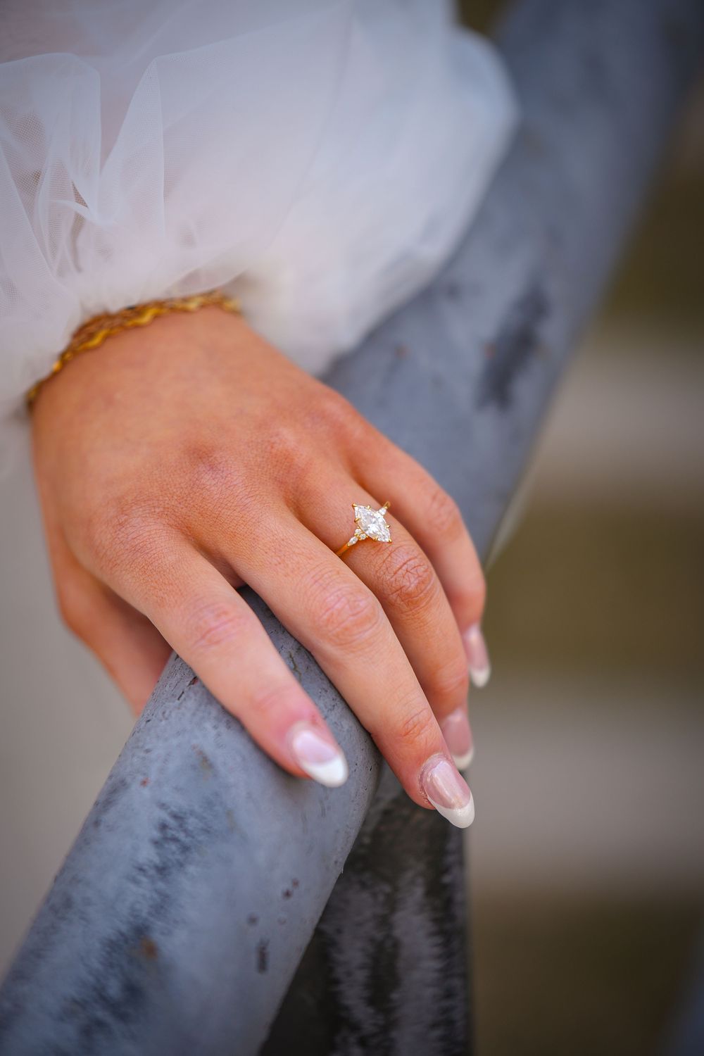 Close-up of a bride's hand wearing a gold diamond engagement ring resting on a gray metal railing.