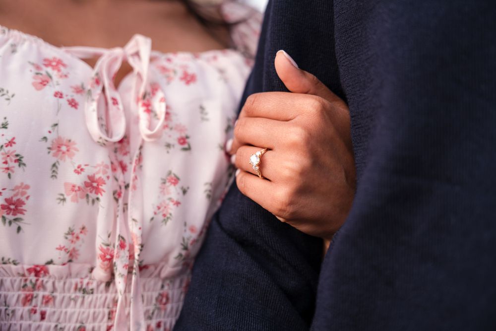 Close-up detail of clasped hands showing a wedding ring against contrasting navy and floral pink clothing.