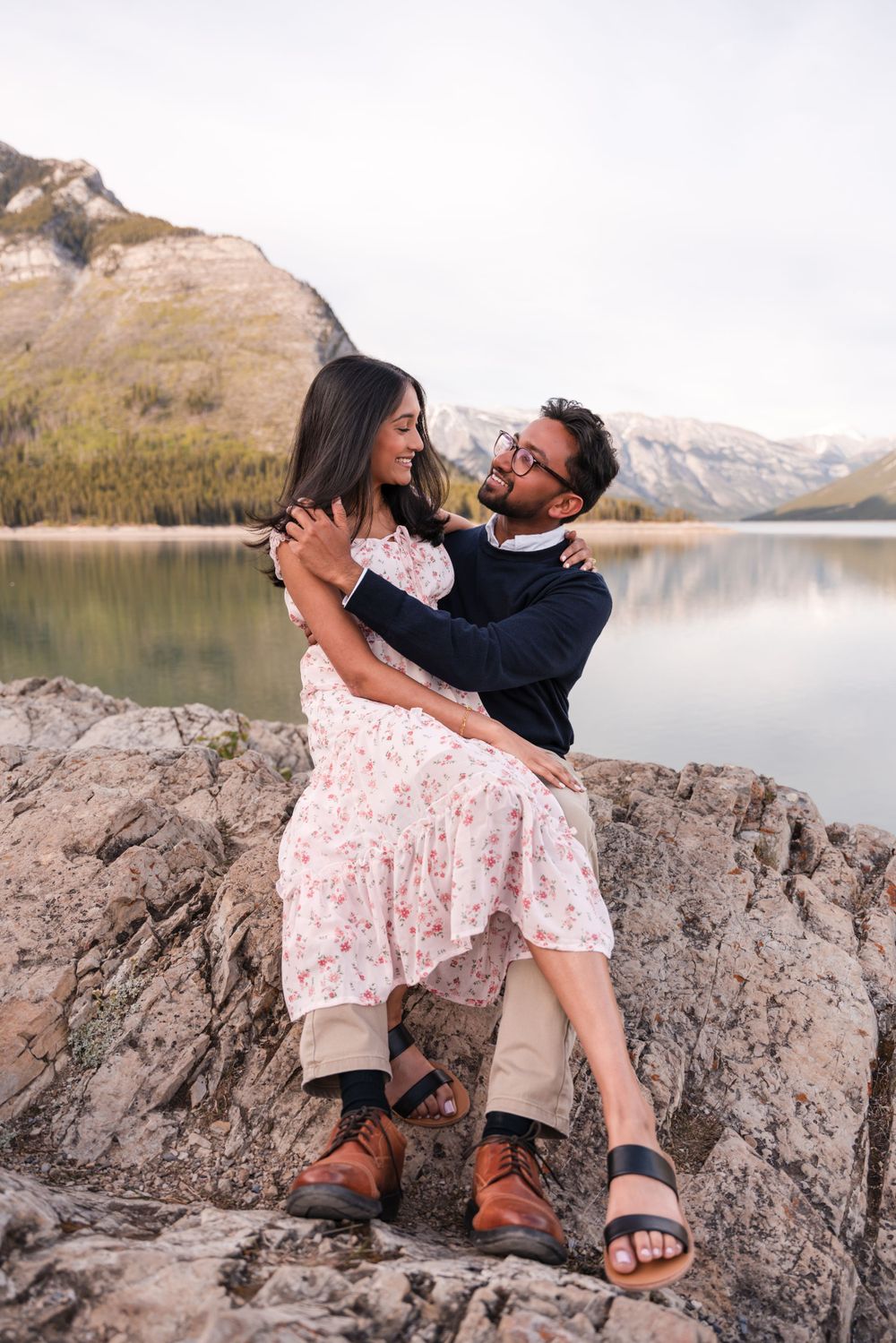 A tender moment shared on rocky terrain overlooking a pristine mountain lake.