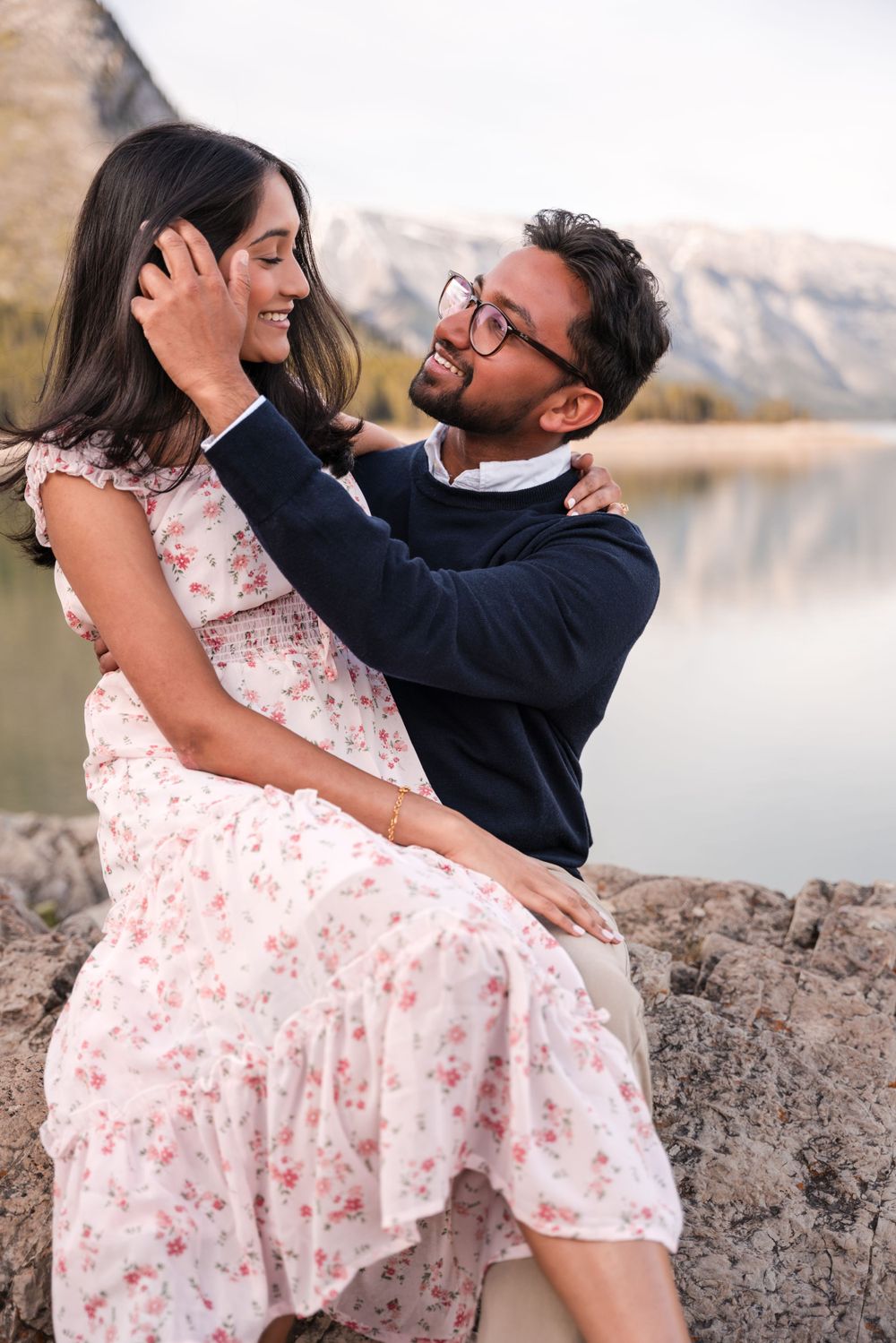 Romantic couple embrace by mountain lake at sunset wearing coordinated navy and floral outfits.