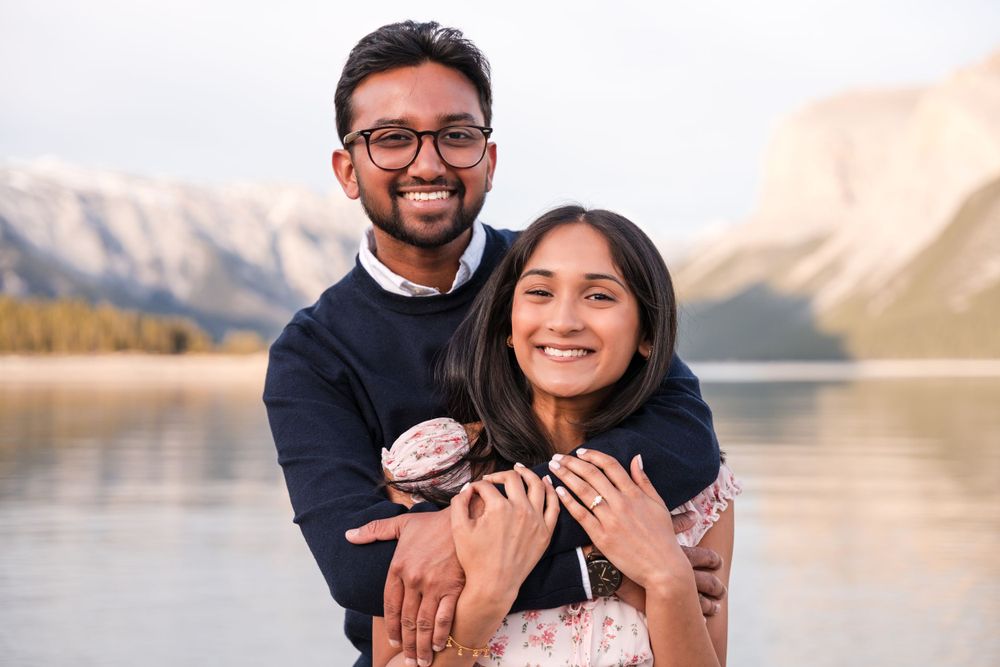 A joyful engagement moment captured against a backdrop of mountains and lake.