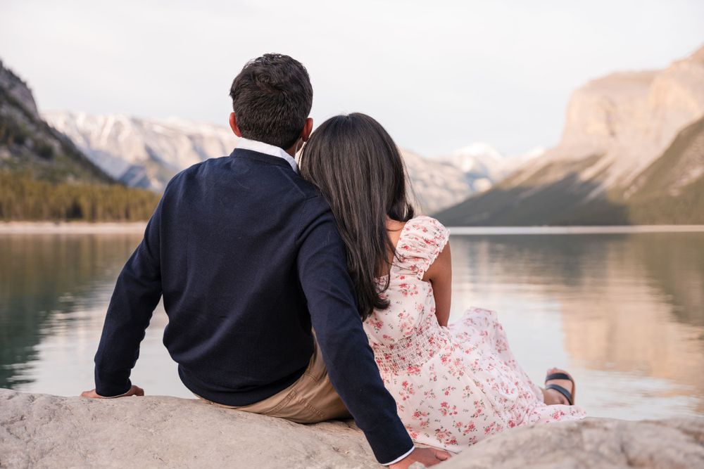 A couple sitting together on a rock overlooking a serene mountain lake during sunset.