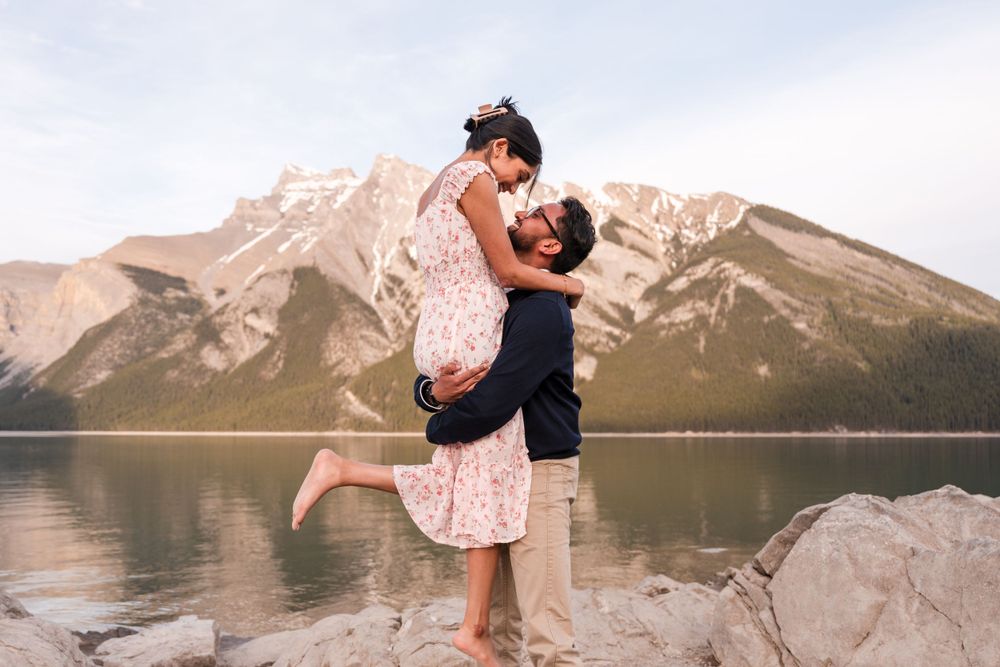 A romantic lakeside scene with a couple embracing against a backdrop of majestic mountain peaks and calm waters.