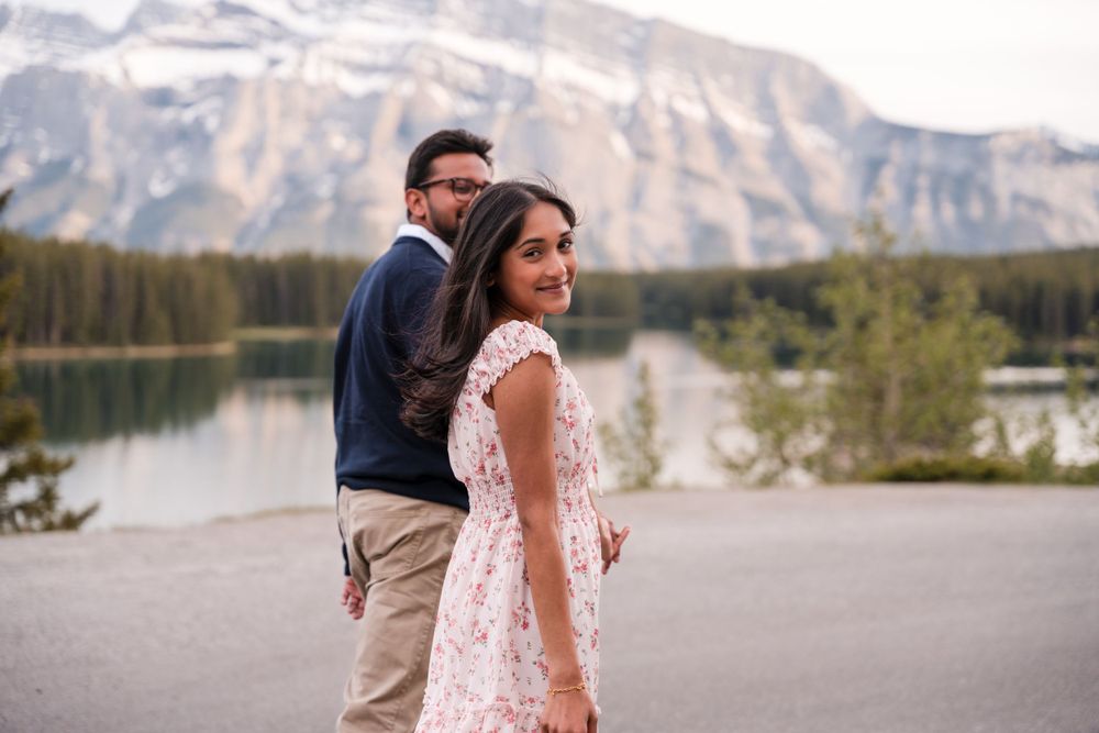 A couple poses together near a scenic mountain lake in a romantic outdoor setting.