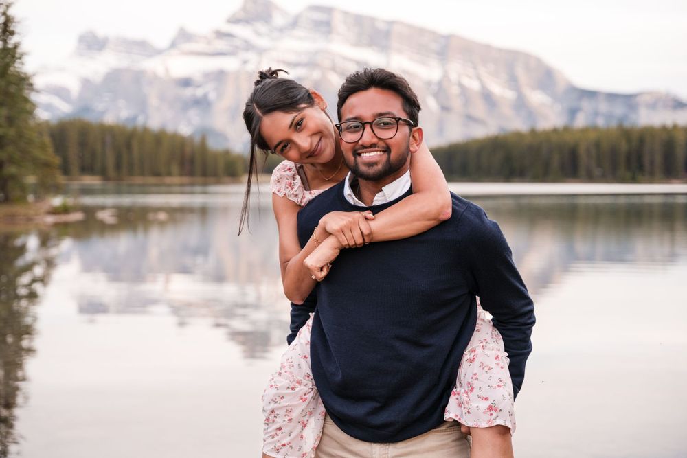 A romantic moment by a serene mountain lake with towering peaks and forests in the background.