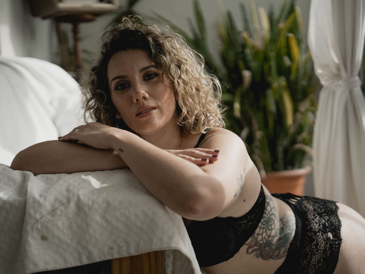 Moody boudoir photograph featuring person in black lingerie near window with plants.