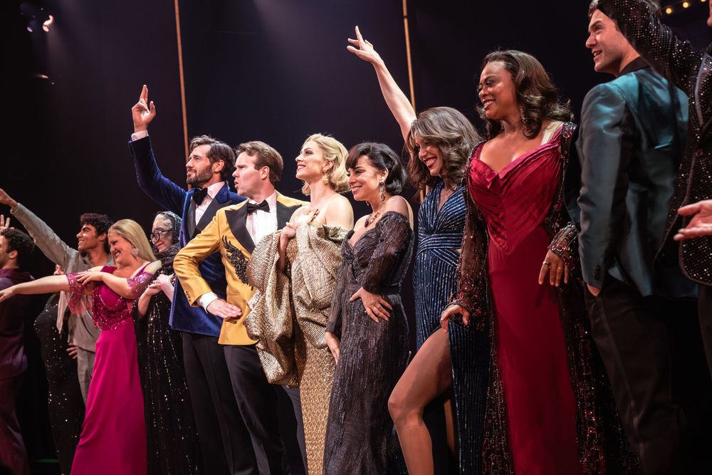 A group of performers take a bow on stage during a theatrical production wearing formal evening attire.