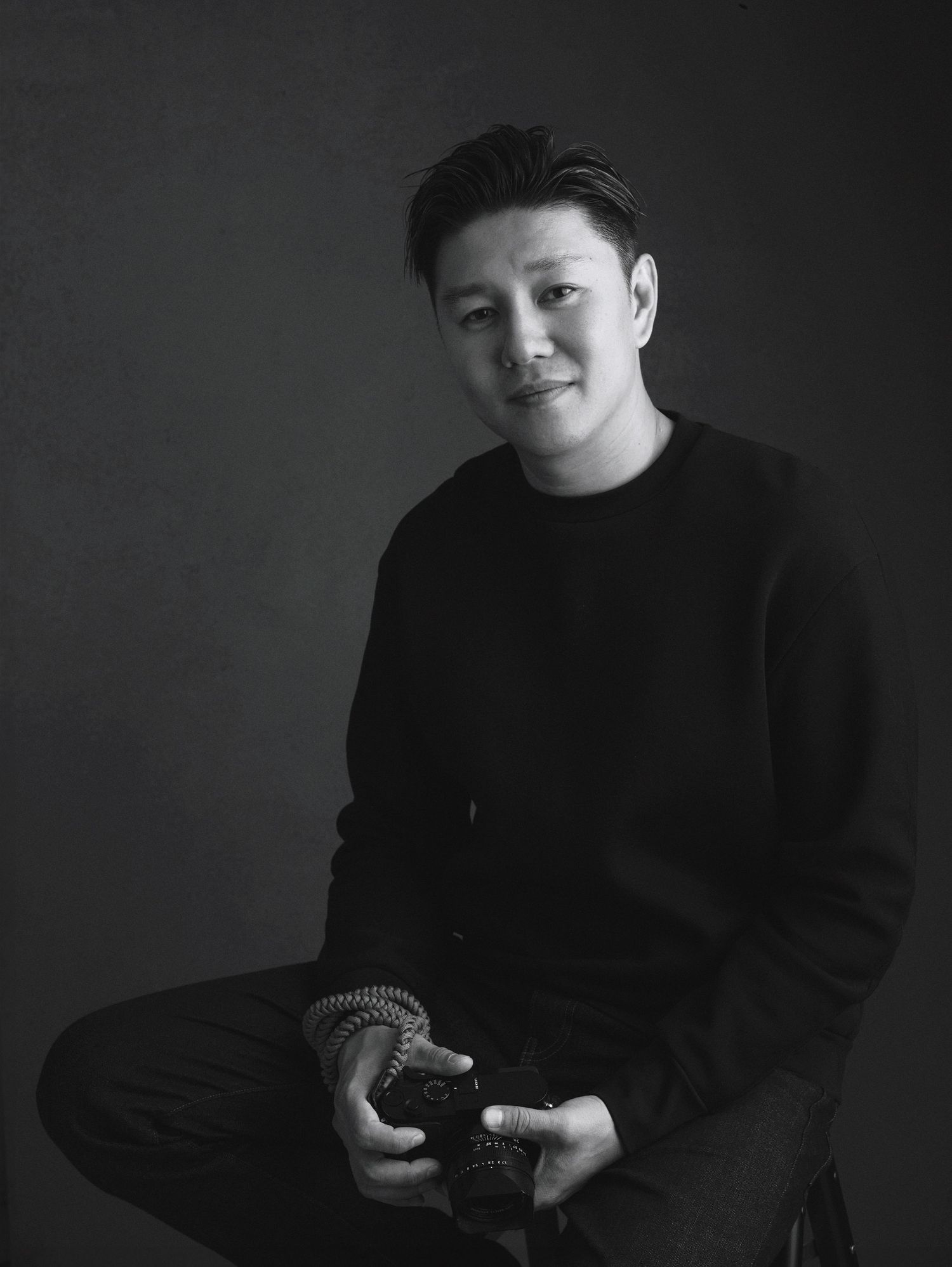 Black and white portrait of KC Chan, a HK based wedding photographer, sitting and holding a Leica Q2 confidently.