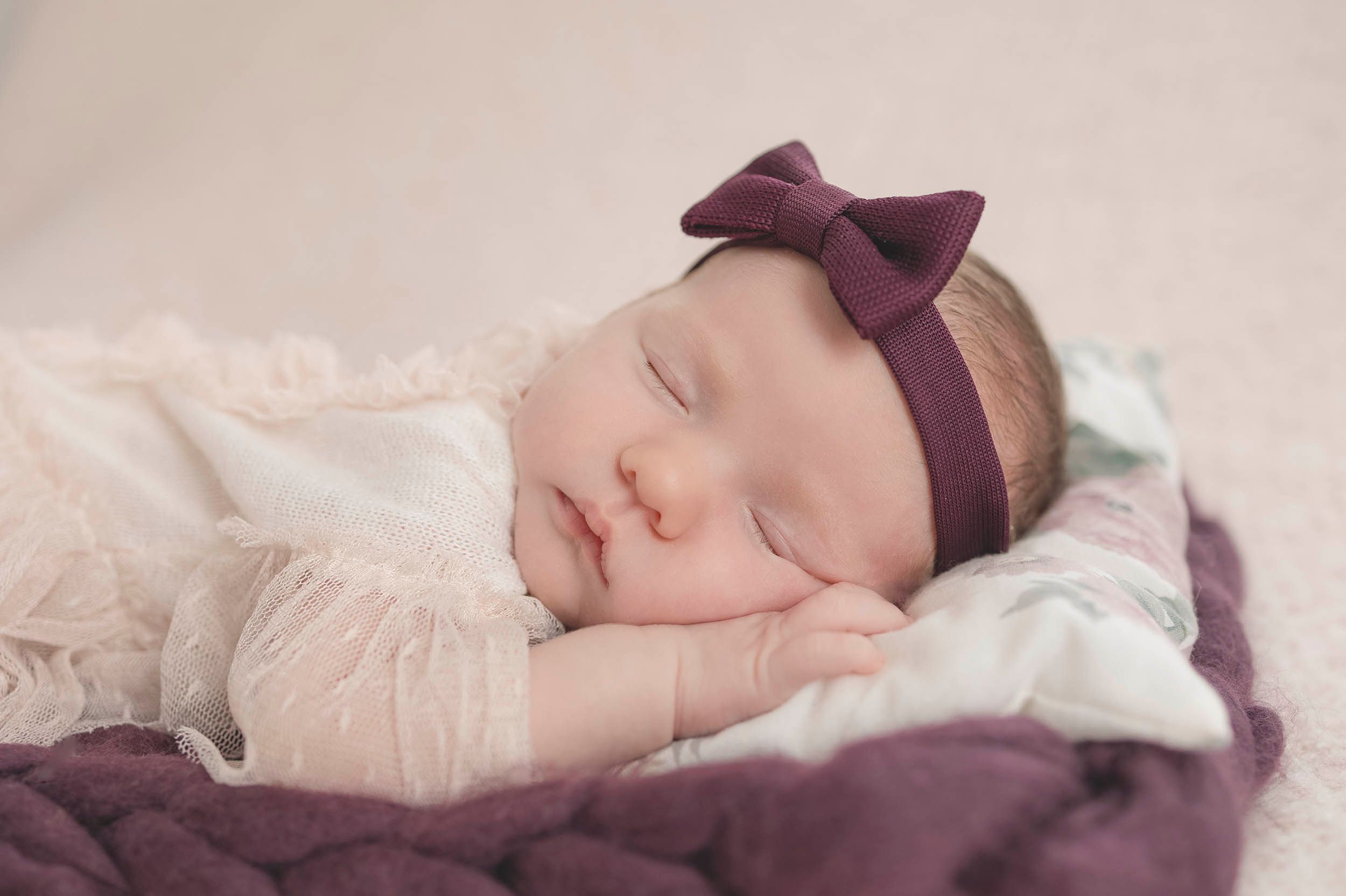 Sleeping baby wearing purple bow headband during peaceful nap. Hampshire newborn photography, Gosport newborn baby photographer, studio