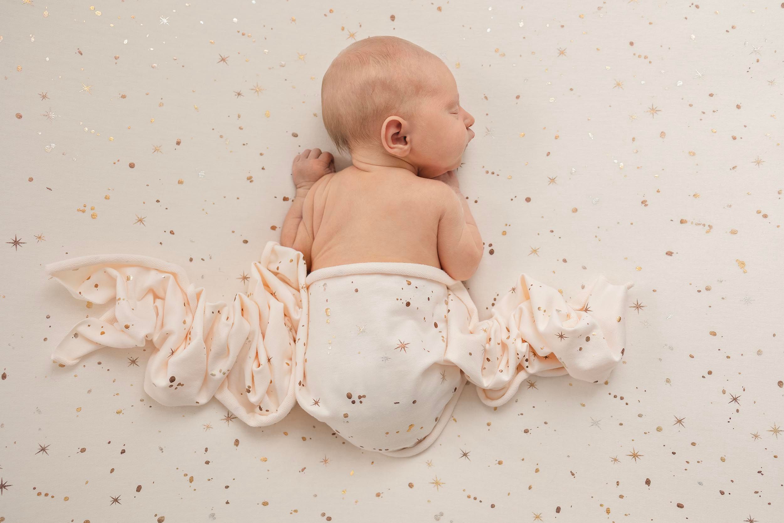 Newborn baby lying on speckled fabric wearing soft pink ruffled fabric. Hampshire newborn photographer, Gosport newborn photography studio