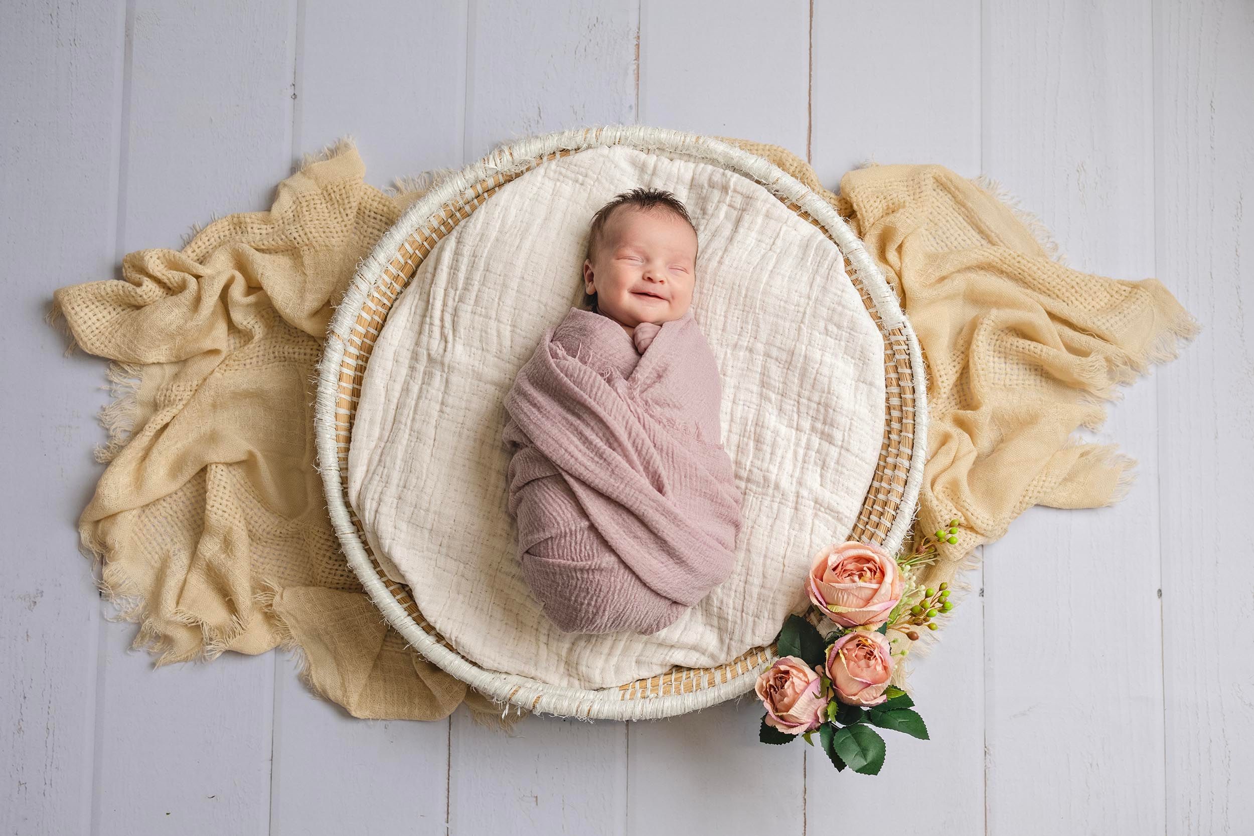 A sleeping newborn baby swaddled in pink lies in a white woven basket and floral accents. Gosport baby photography, fareham newborn photo