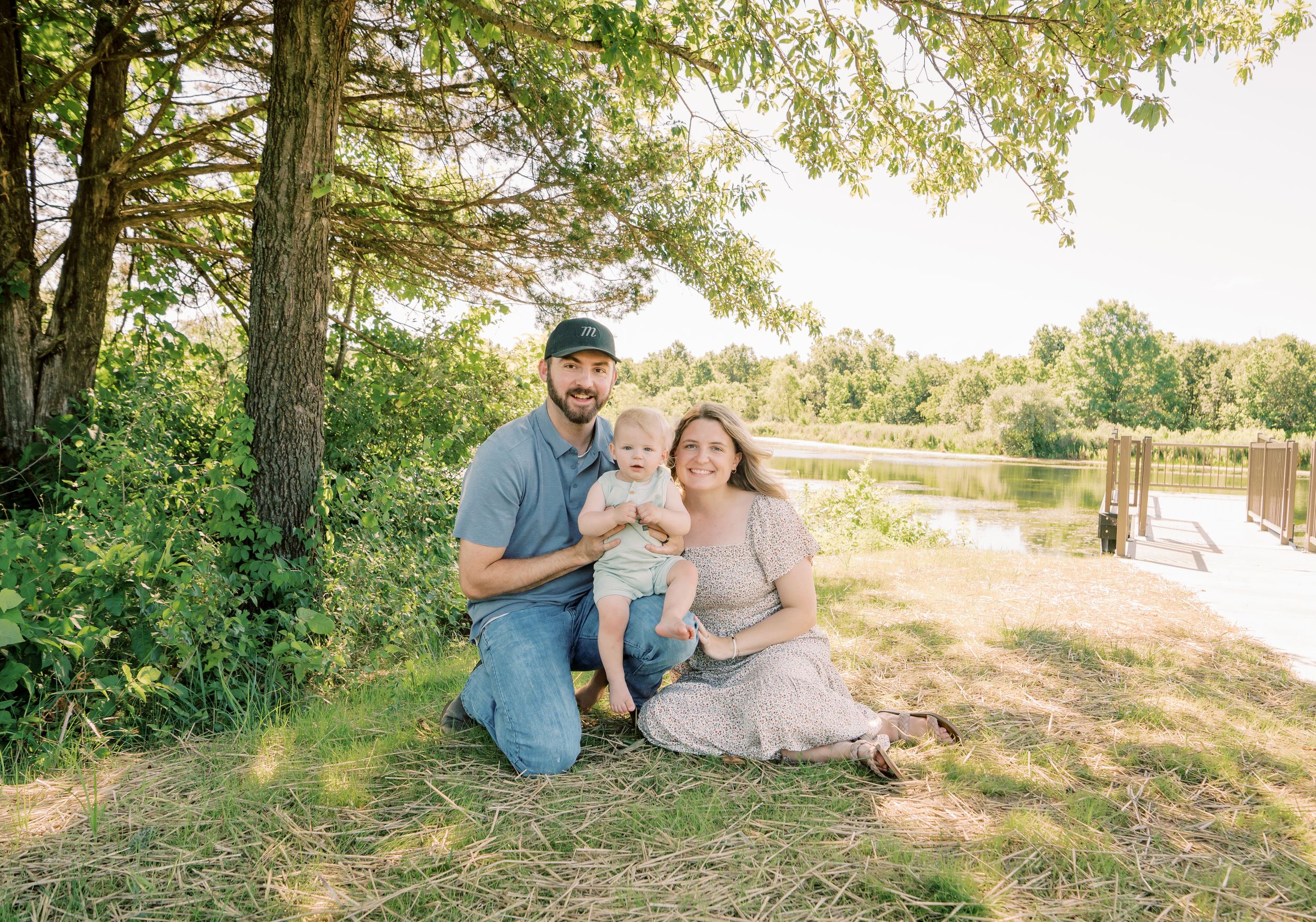Family of three sitting together under a tree by a peaceful lake in Columbia, MO, capturing a serene and loving moment in nature