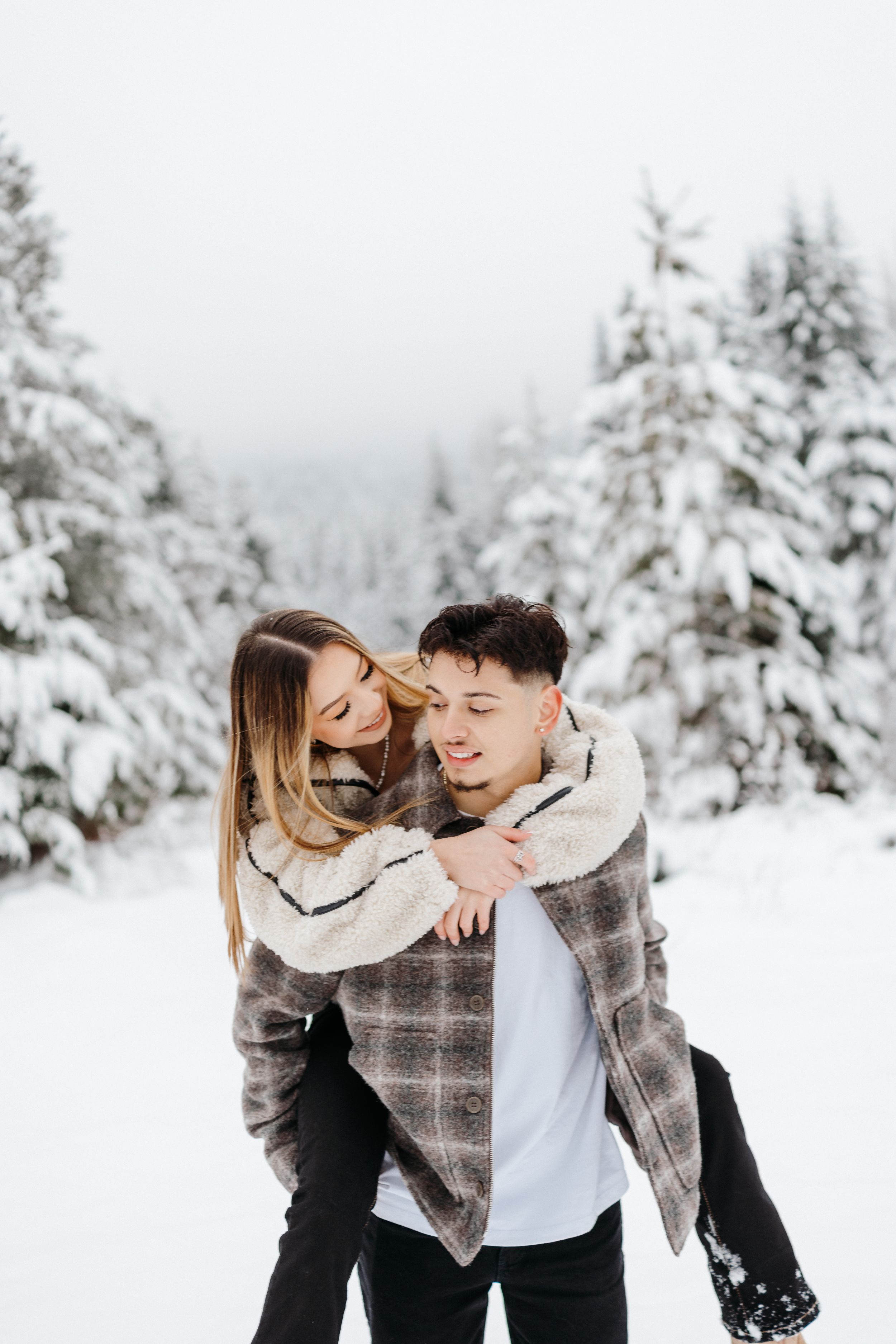 A playful winter scene with two people sharing laughter in a snowy evergreen forest setting.