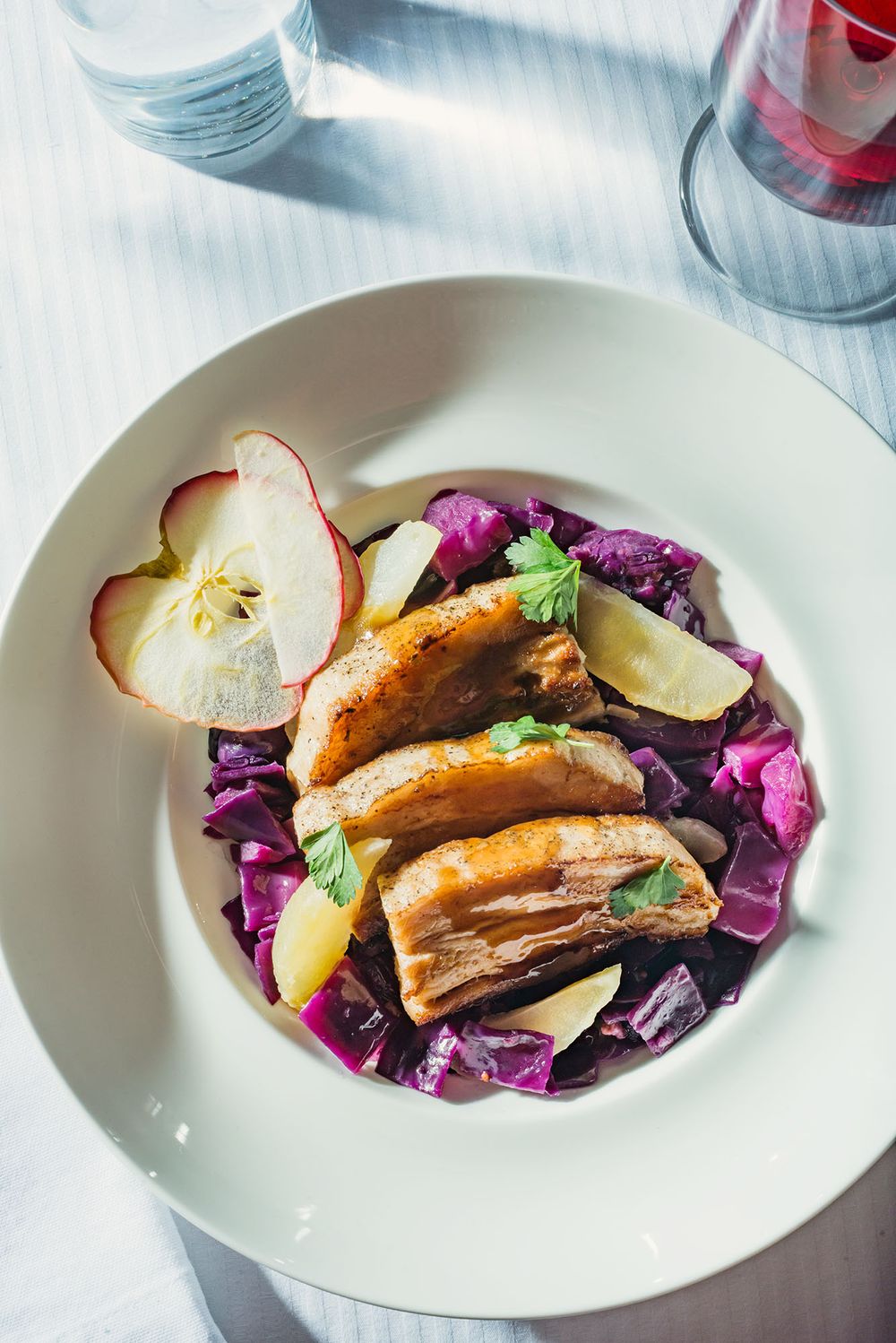 Roasted pork ribs served on braised red cabbage with apple slices and fresh herbs on a white plate.