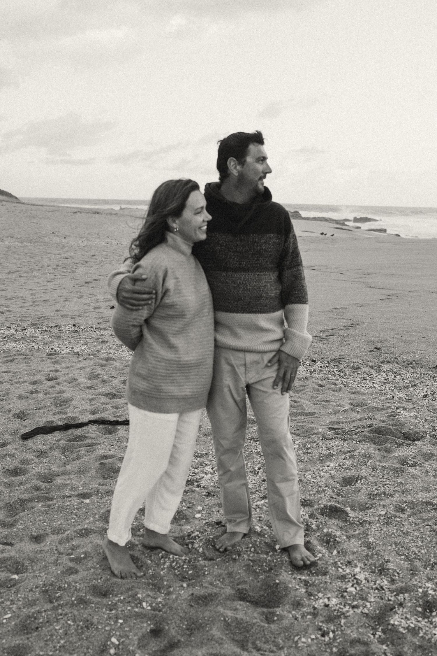 Couple walking together along a scenic beach shoreline in matching sweaters.