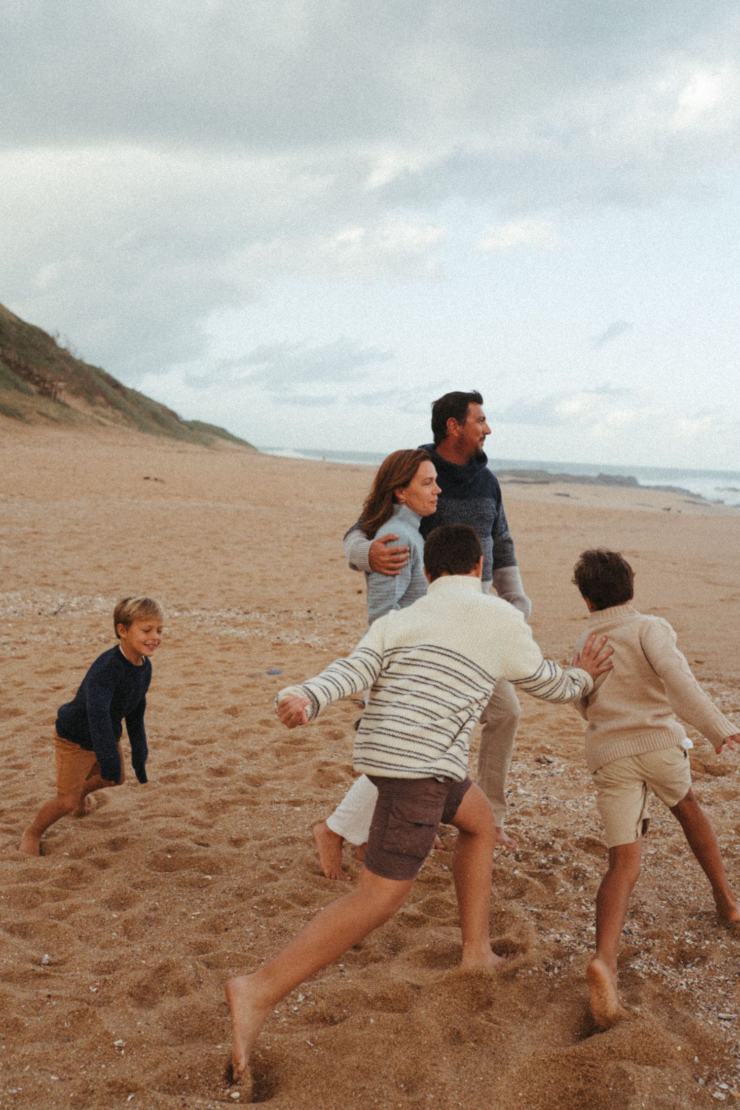 Playful group running and jumping on a sandy beach under cloudy skies.