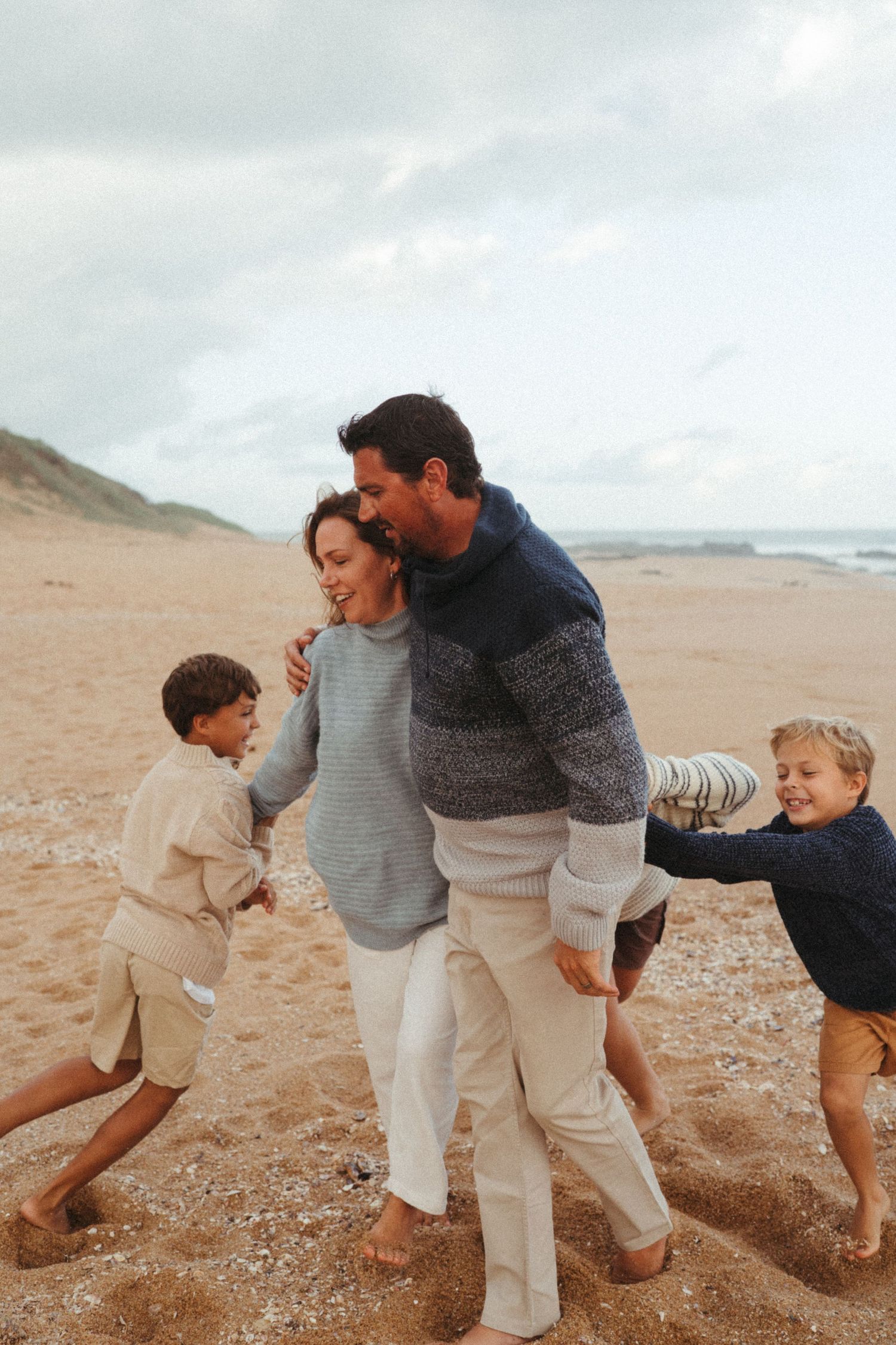 Family playing chase games together on a cloudy beach.