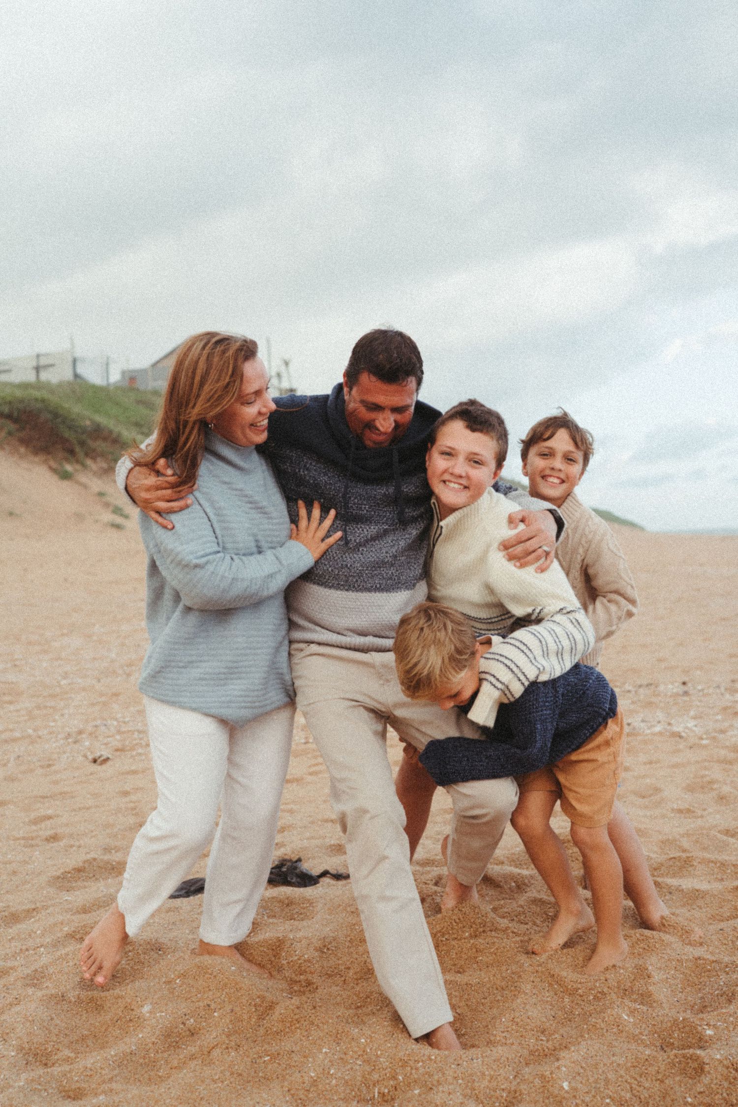 Family sharing joyful moments and embraces on a cloudy beach.