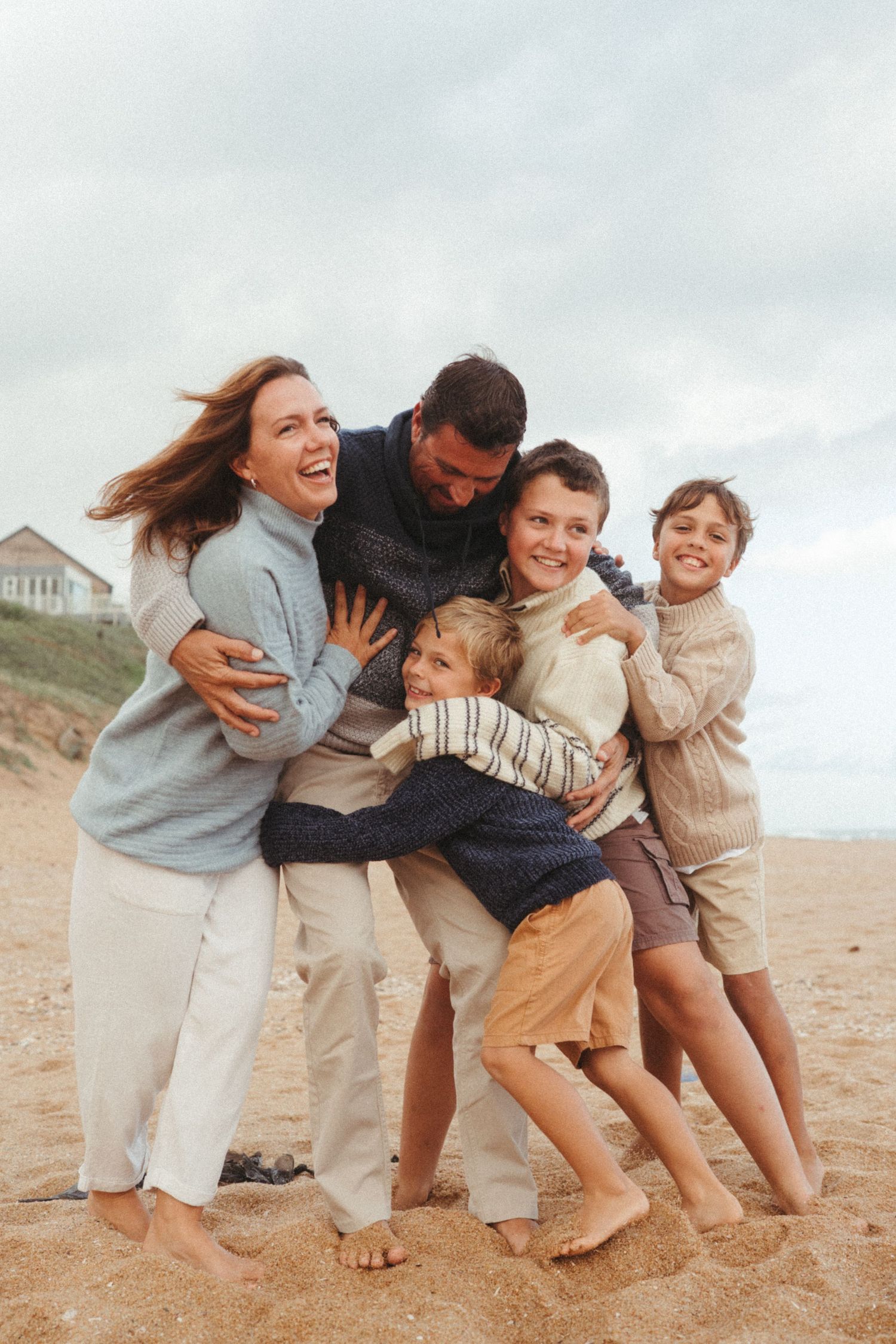 Family members in casual beach attire sharing an affectionate group hug on the sand.