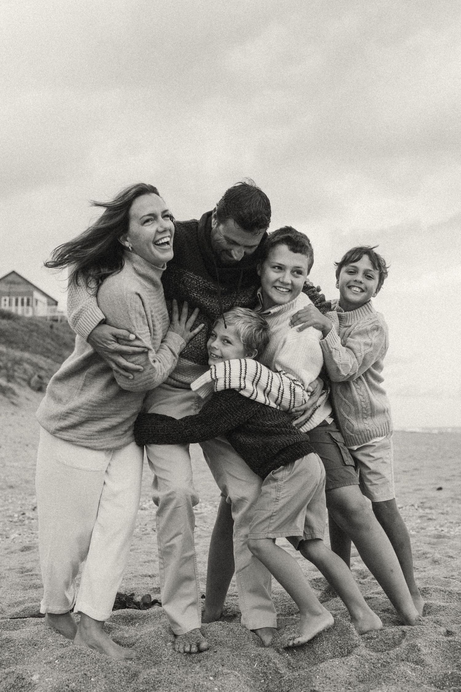 A joyful family playing and hugging together on a sandy beach on an overcast day.