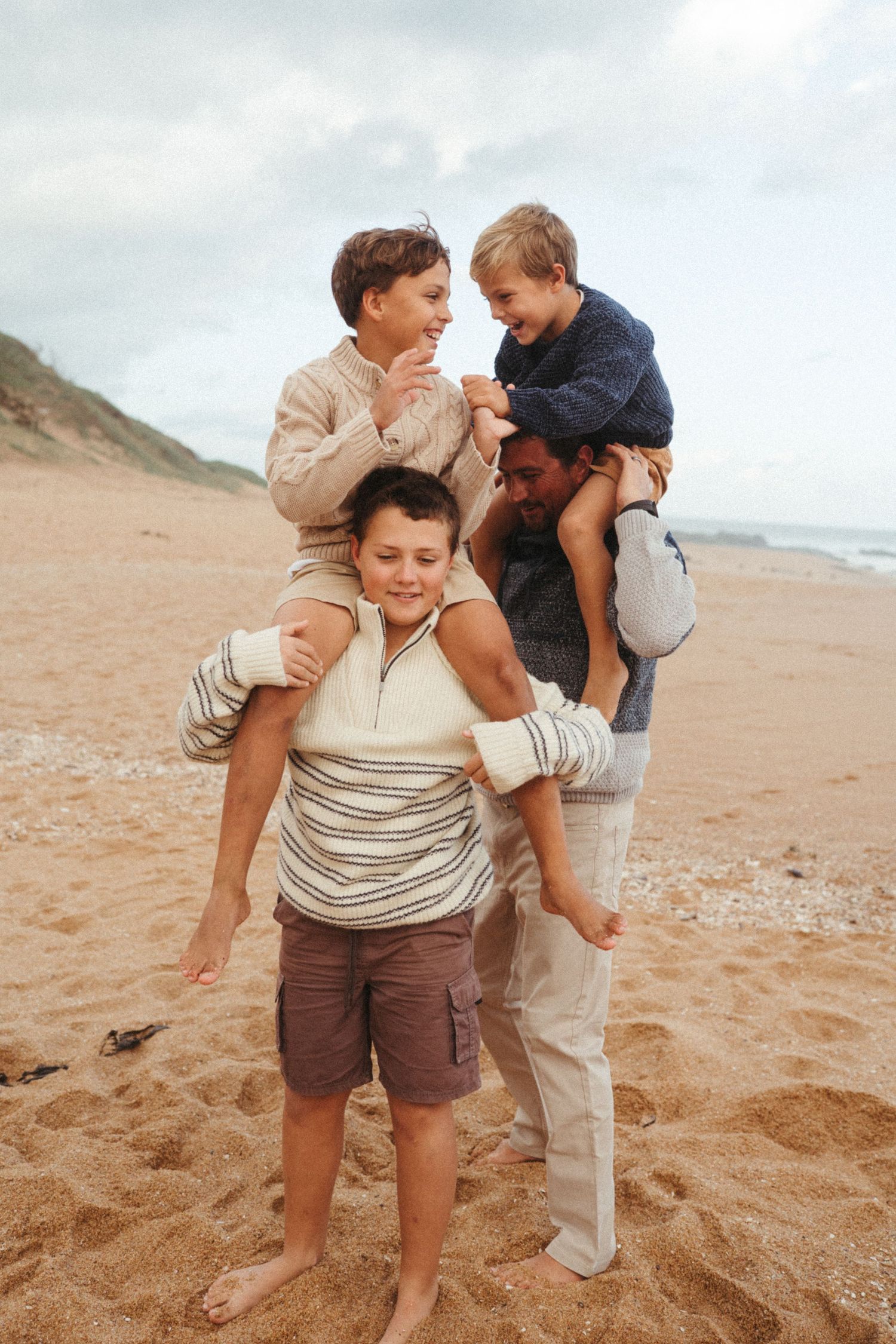 Playful family members giving piggyback rides and laughing on a beach.