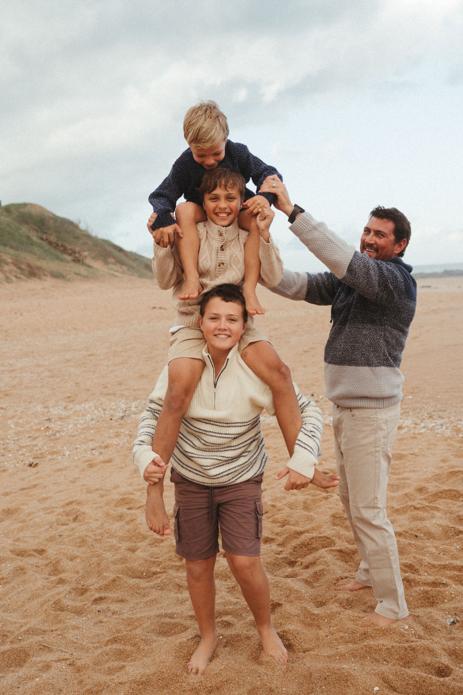Family members playing and carrying each other on their shoulders at the beach.