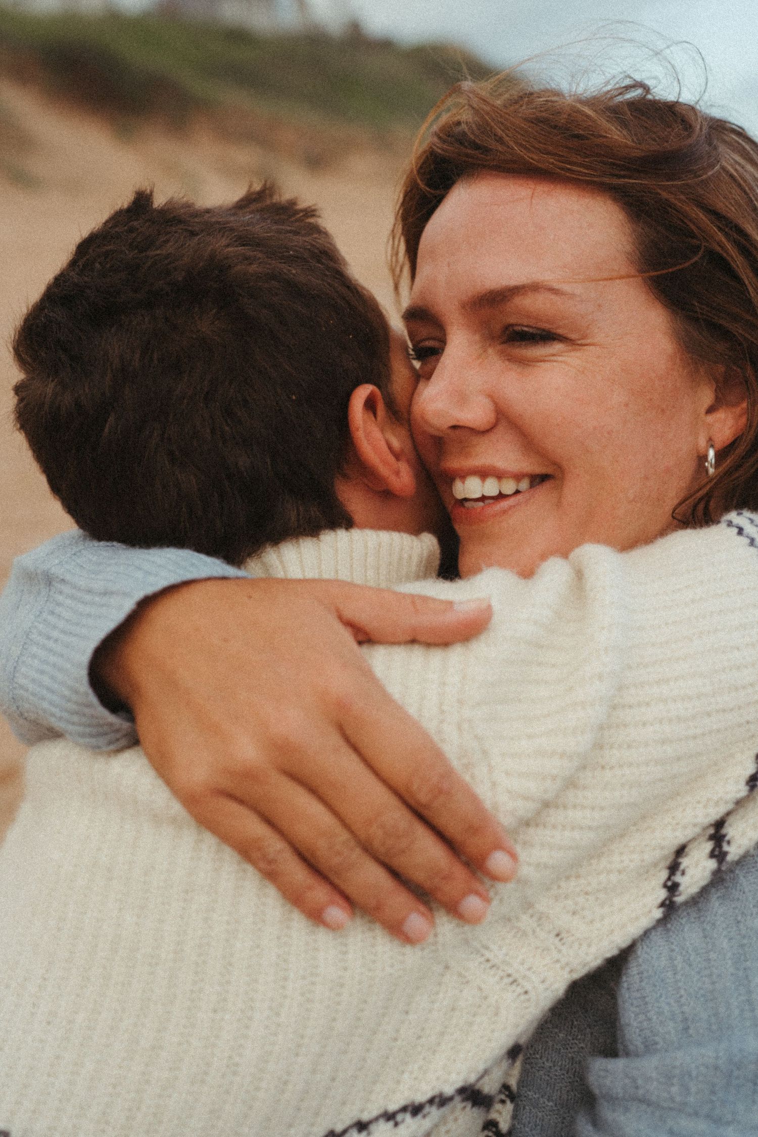 Intimate embrace between two people wearing white and gray sweaters on a sunny day.