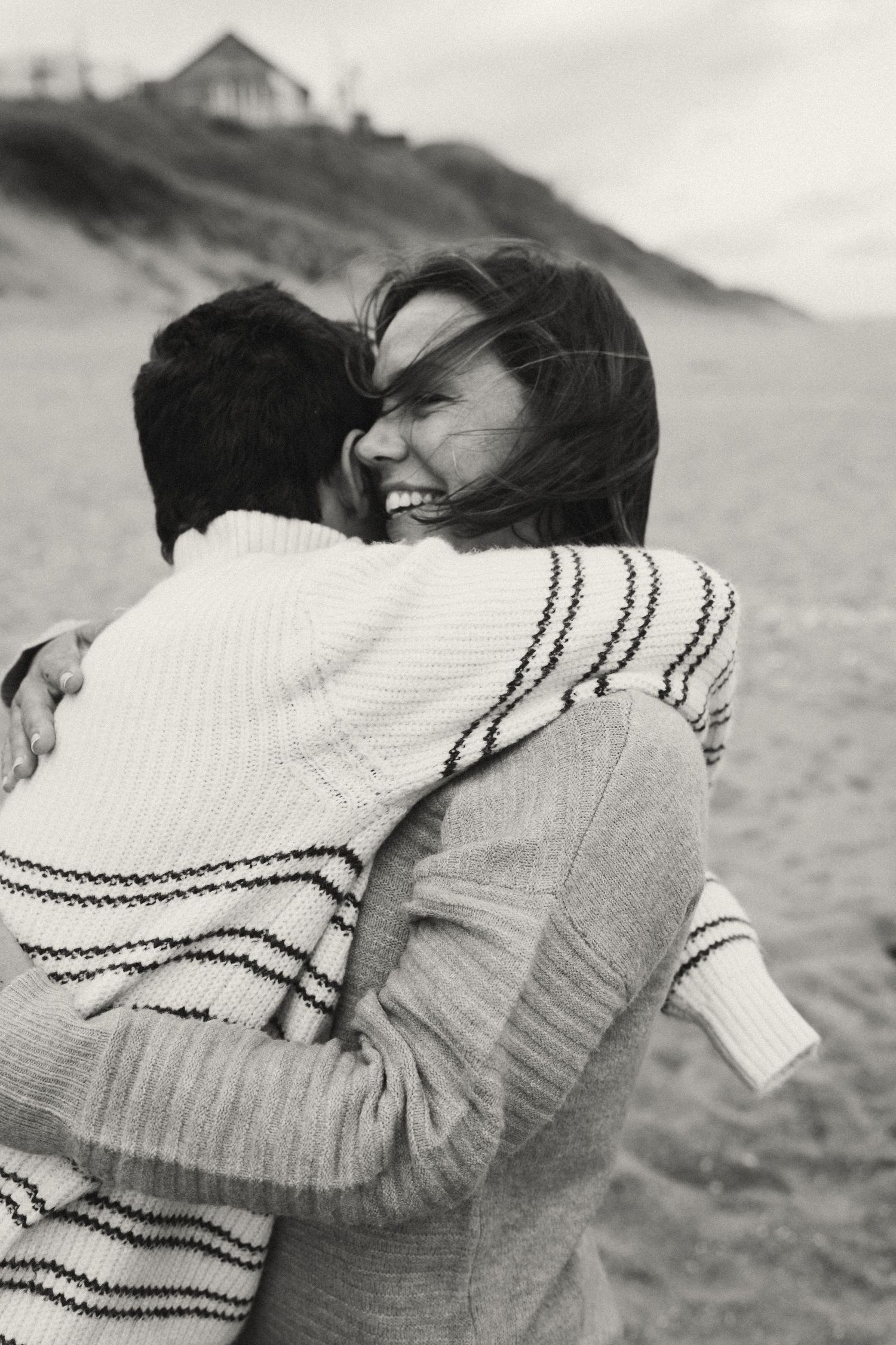 Black and white beach photo showing an emotional embrace in cozy sweaters.