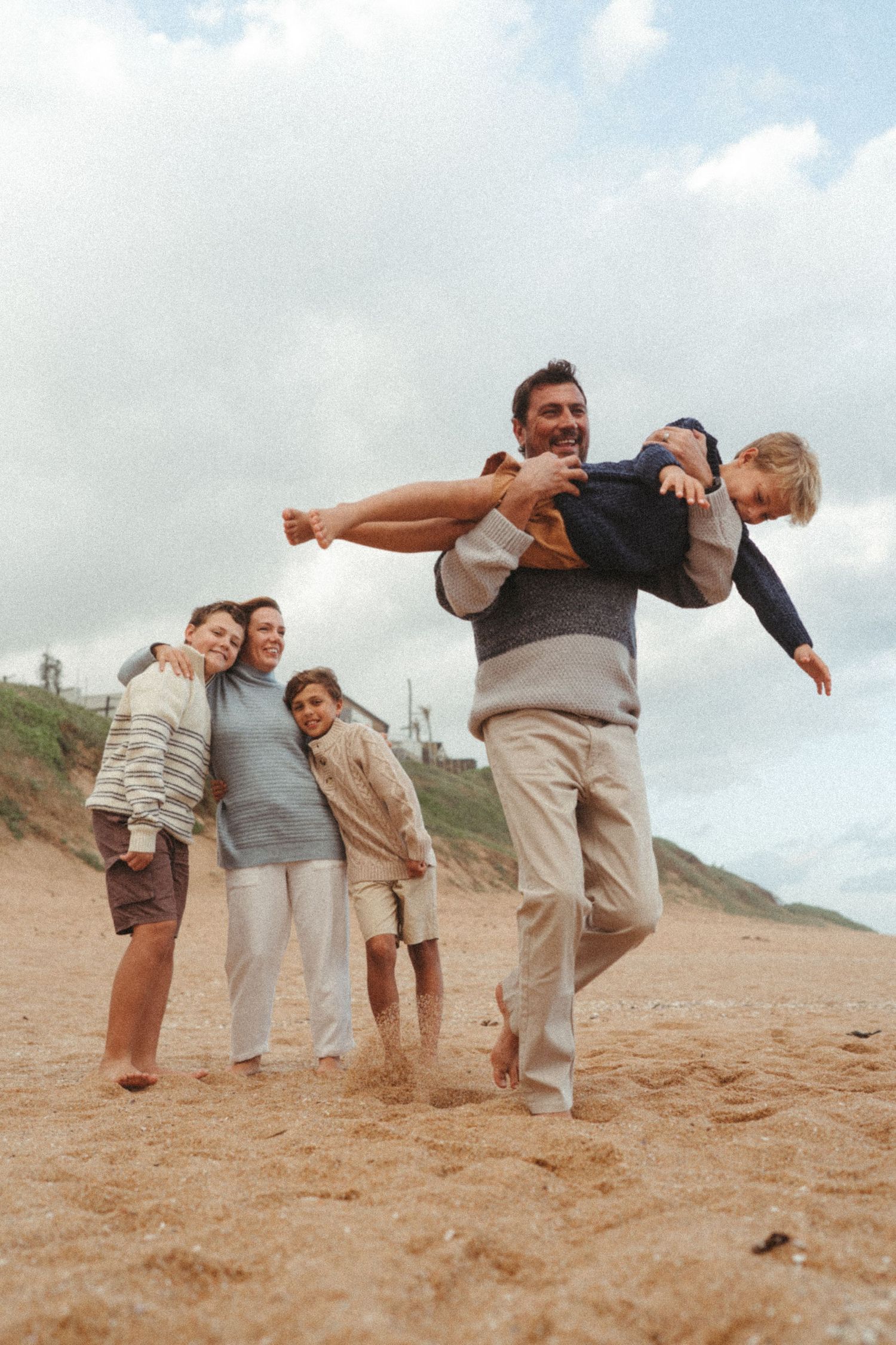 Group of people playing and posing together on a sandy beach under cloudy skies.
