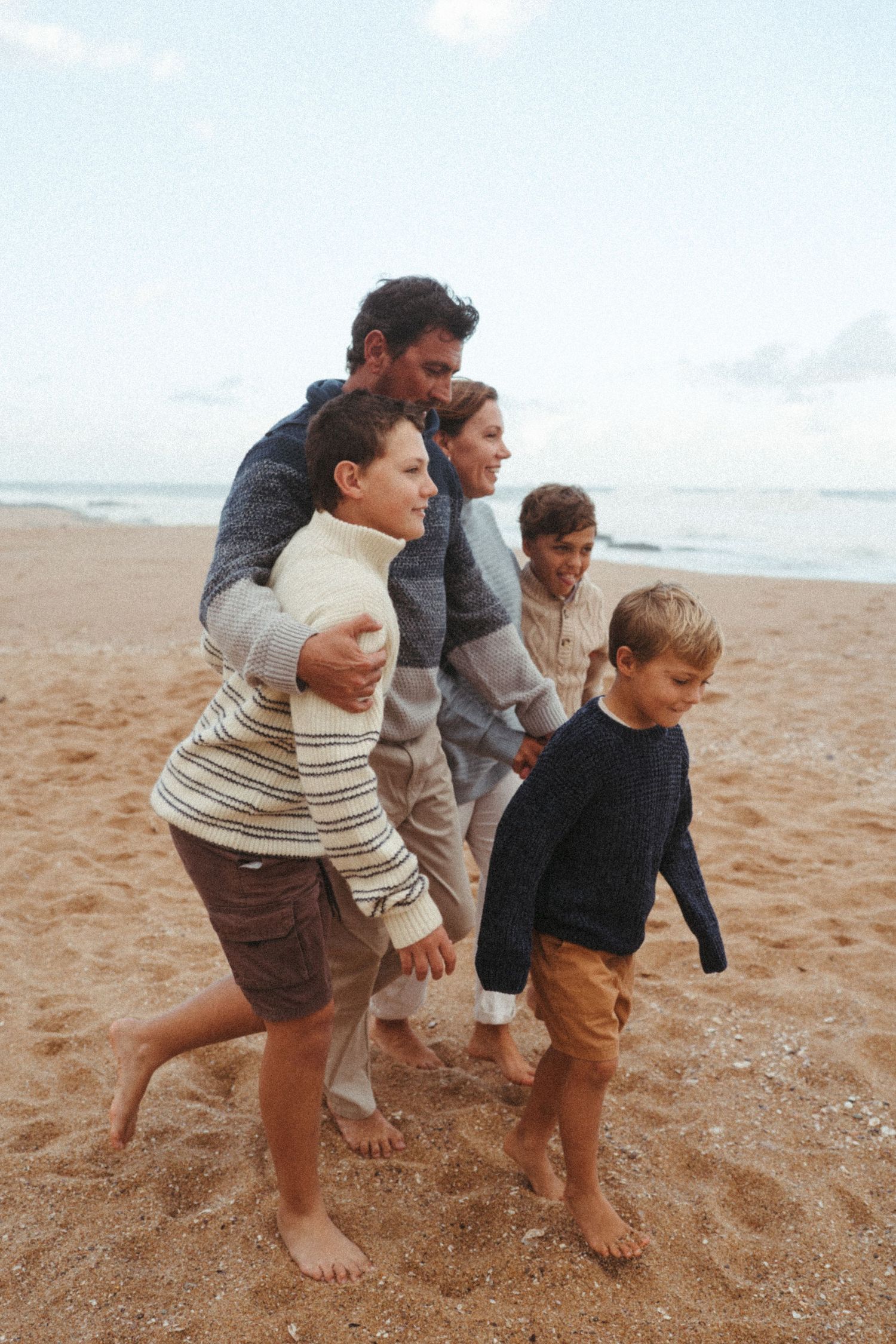 People running and playing together barefoot on a sandy beach.