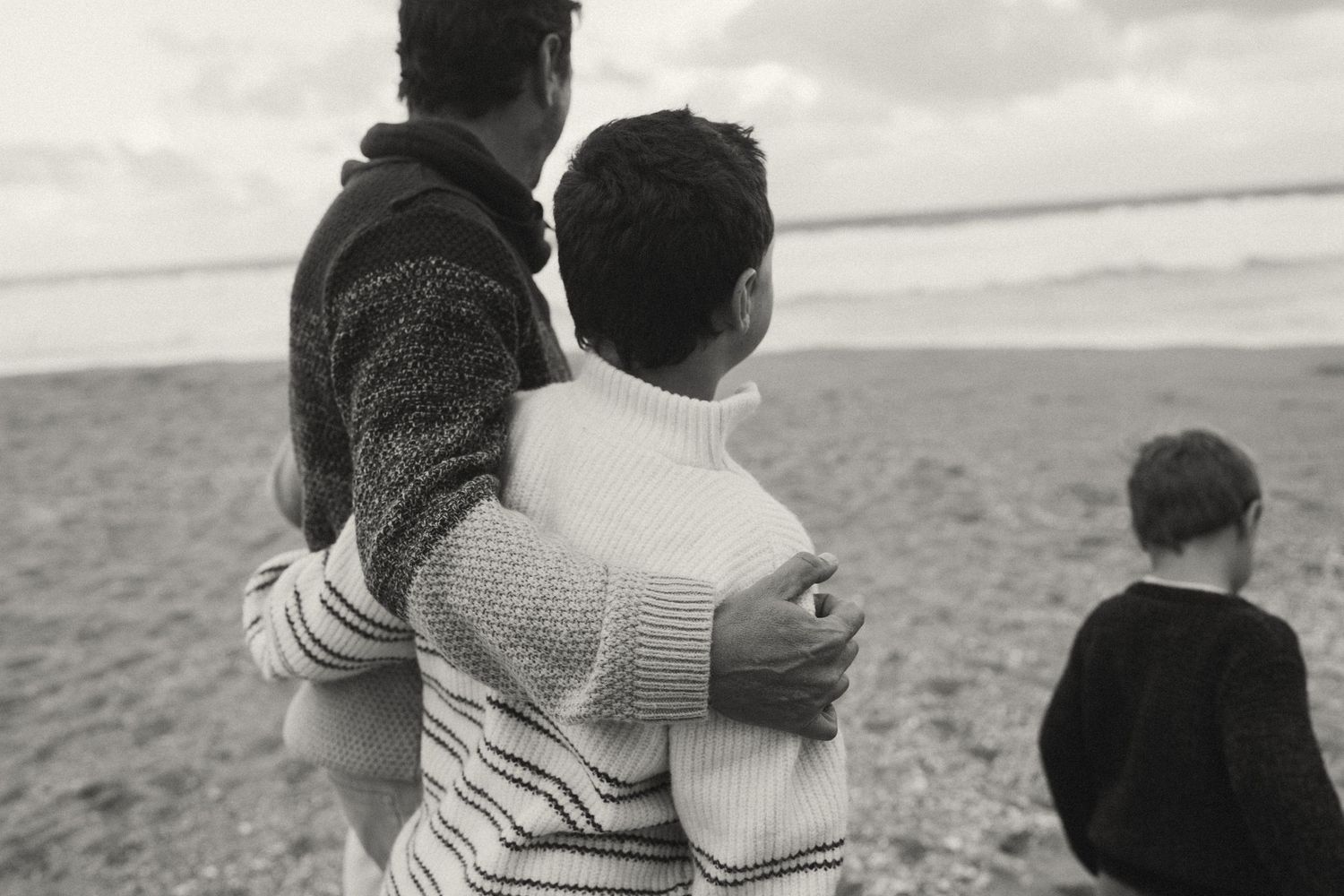 A group lounges together on a sandy beach with cliffs in the background, captured in black and white.
