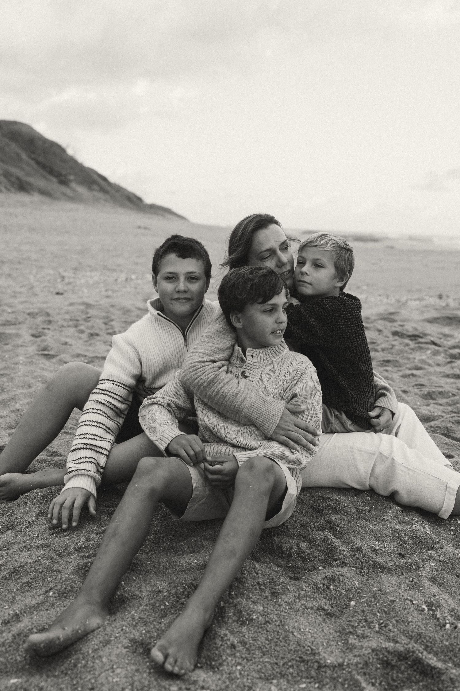 A group lying together on a sandy beach slope in black and white.