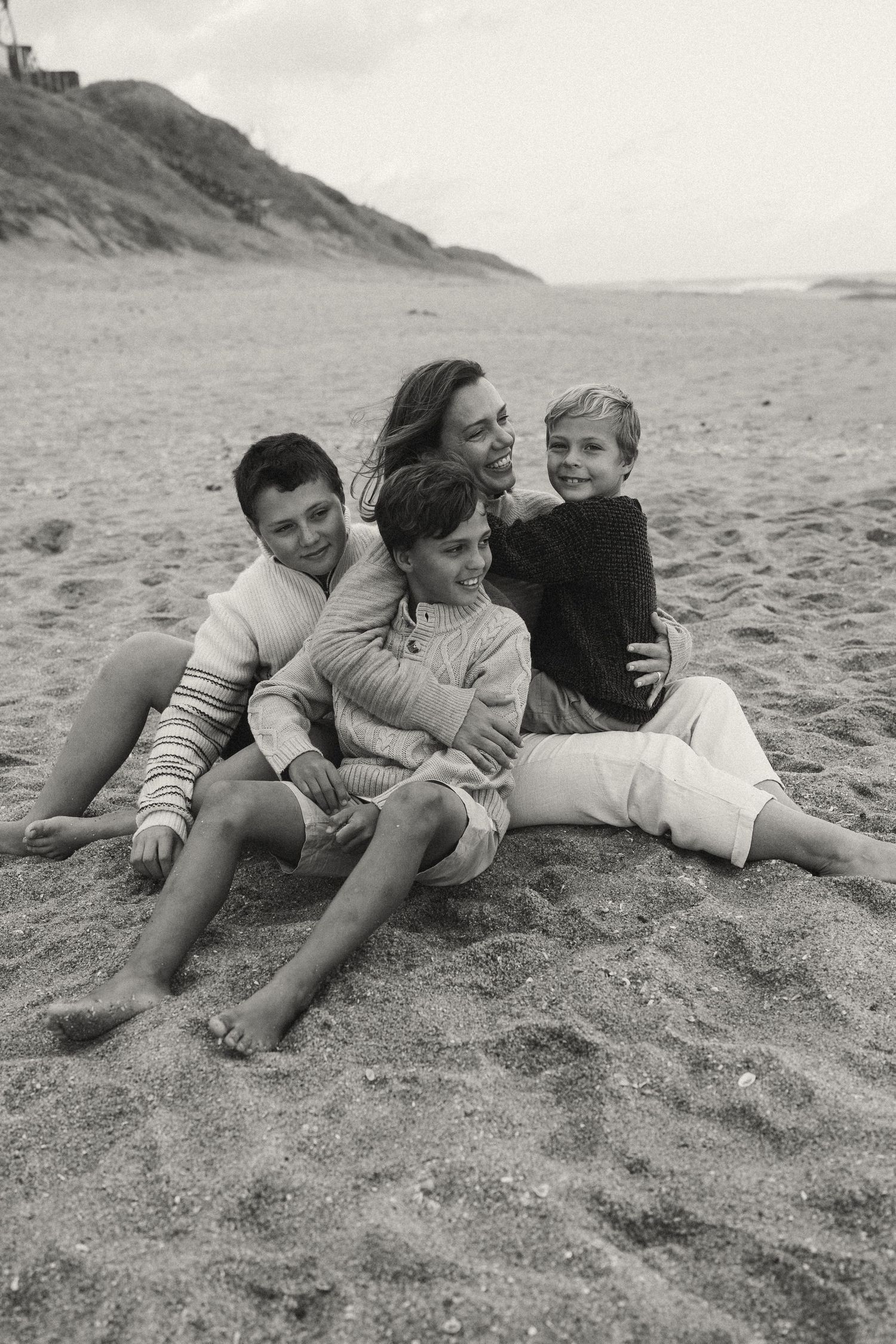 People relaxing on a sandy beach with coastal cliffs visible in monochrome.