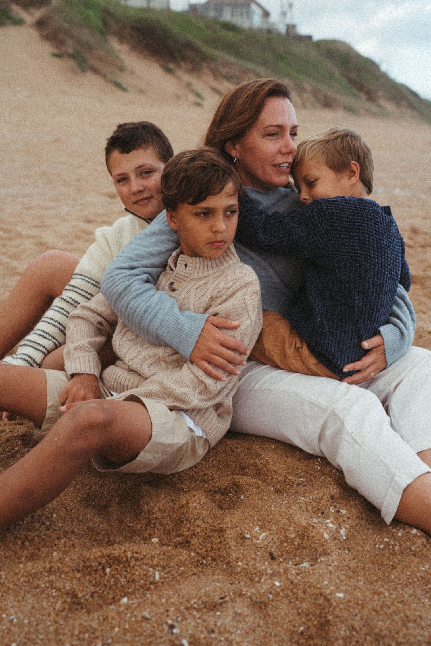 People snuggle close together while lying on a sandy beach slope.