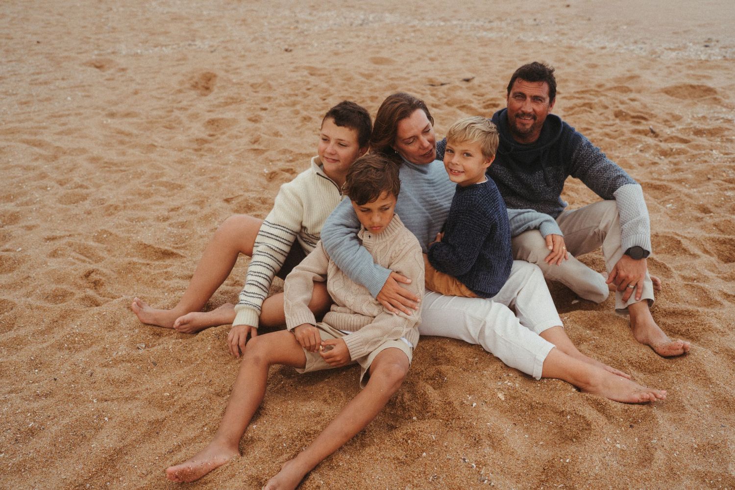 A group cuddles together while relaxing on warm beach sand.