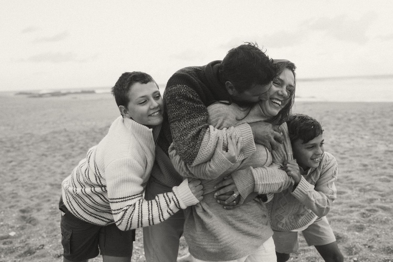 Group embracing in laughter on a sandy beach.