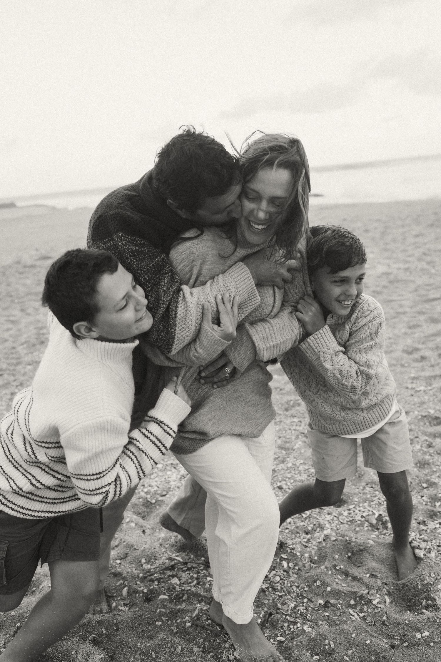 Friends playing and embracing on a cloudy beach day.