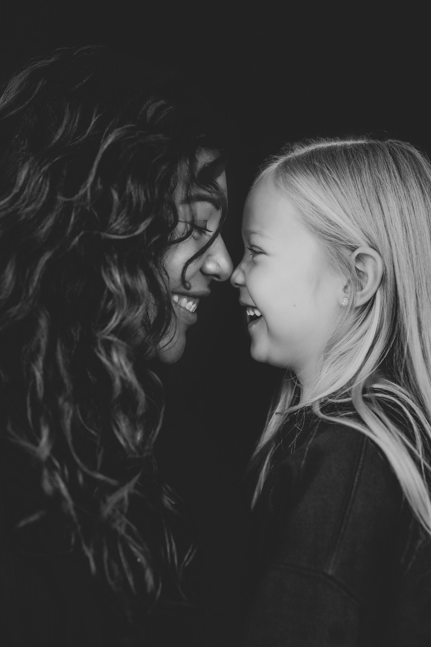 Black and white photo of a woman and young girl smiling face to face, sharing a joyful moment together.