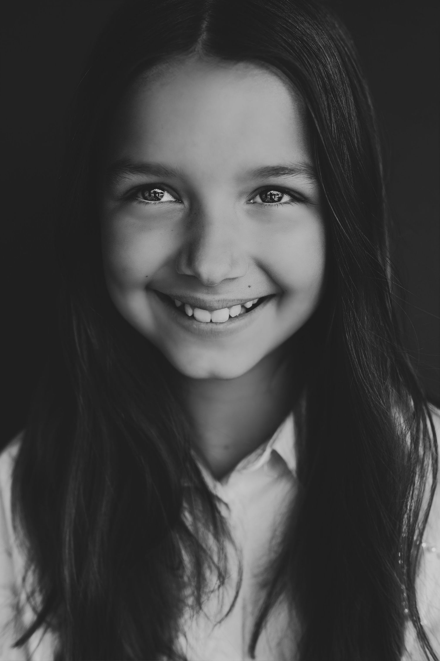 Black and white portrait of a smiling young girl with long dark hair wearing a collared shirt.