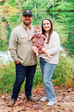 A family poses together by a reflective pond surrounded by autumn foliage.