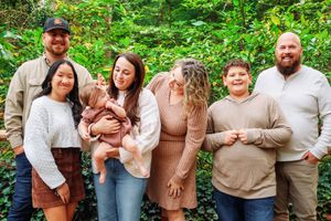 A group photo of family members in casual attire against a lush green forest backdrop.