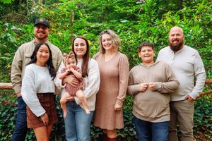 A group family photo captured outdoors with a backdrop of green forest vegetation.