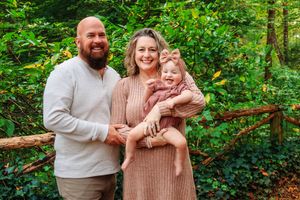 A family portrait taken in a forest setting with natural green foliage in the background.