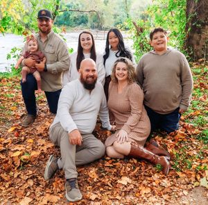 A family group poses together on fallen autumn leaves in an outdoor setting.