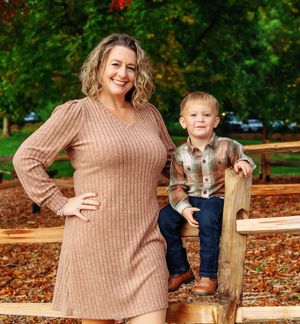 An outdoor autumn portrait by a wooden fence with fallen leaves.