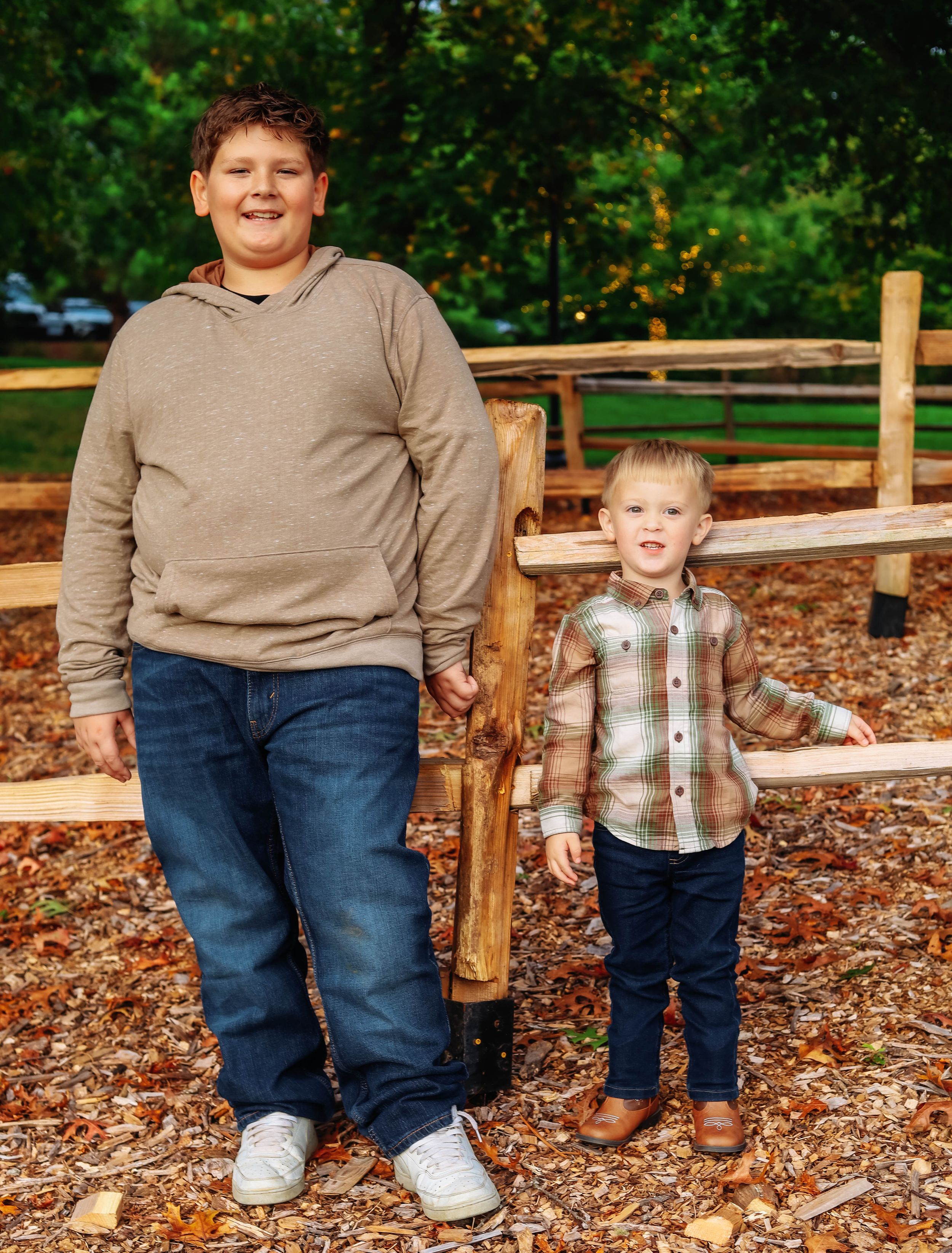 Two people stand together by a wooden fence in an autumn setting.