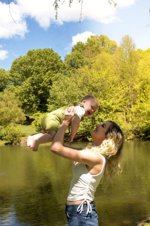 A joyful outdoor moment by a pond on a sunny day with lush green and yellow trees in the background.