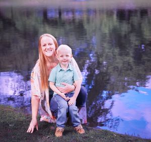 Parent and child sharing playful moment by reflective pond at sunset.