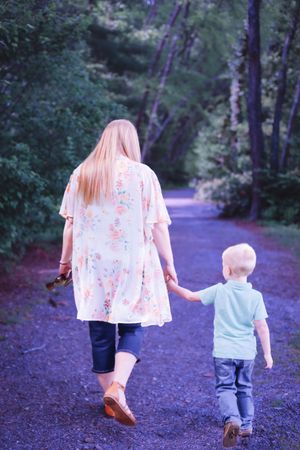 Parent and child walking together on wooded path in evening light.