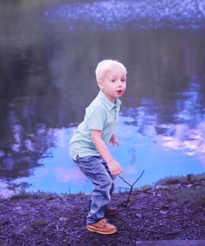 Small child exploring near peaceful pond with purple reflections.